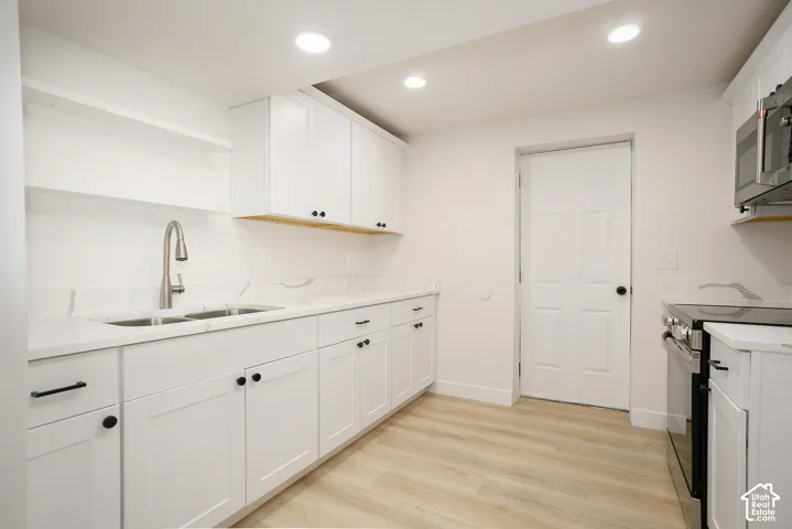 Kitchen featuring white shaker-style cabinetry, stone-finish countertops, stainless steel appliances, a pull-down faucet, and wood-finish flooring
