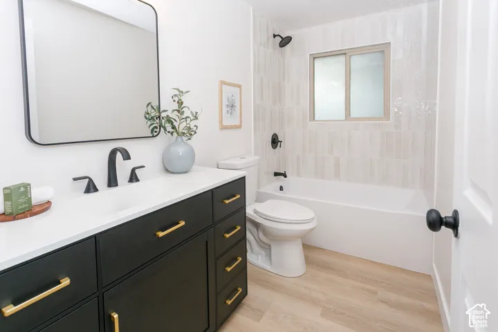 Black vanity cabinet featuring brass hardware and a white countertop with an integrated sink, rectangular mirror with a black frame, wood-finish flooring, and a bathtub with vertical tile surround and matte black fixtures