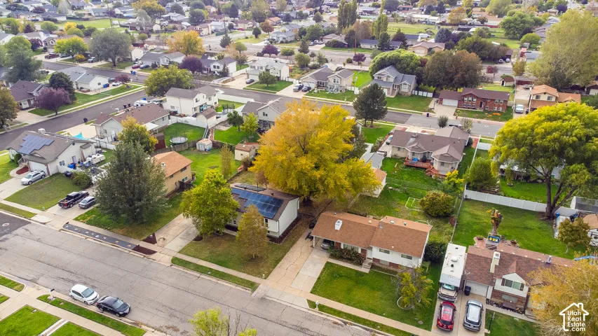 Aerial perspective of a residential property featuring a shingle roof, roof-mounted solar panels, an attached garage, and mature trees