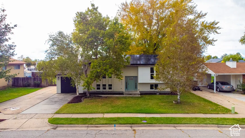 Exterior featuring split-level architecture, solar panels, attached single-car garage, covered carport, and mature landscaping