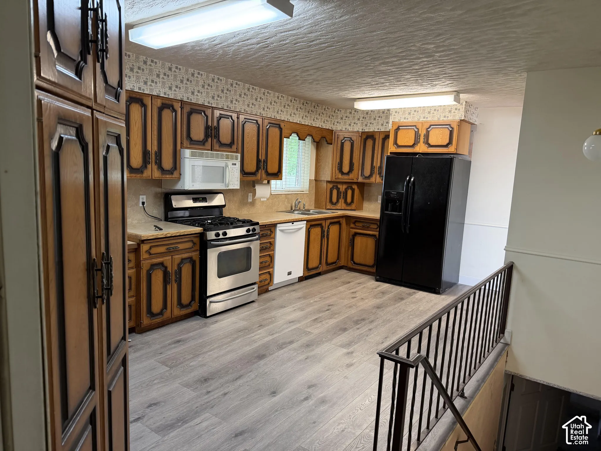 Kitchen featuring wood-finish cabinetry, stainless steel gas range, built-in microwave, wood-finish flooring, and metal railing