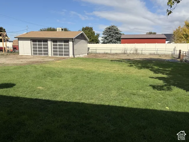 Expansive backyard featuring a manicured lawn, detached two-car garage, and solid vinyl perimeter fencing