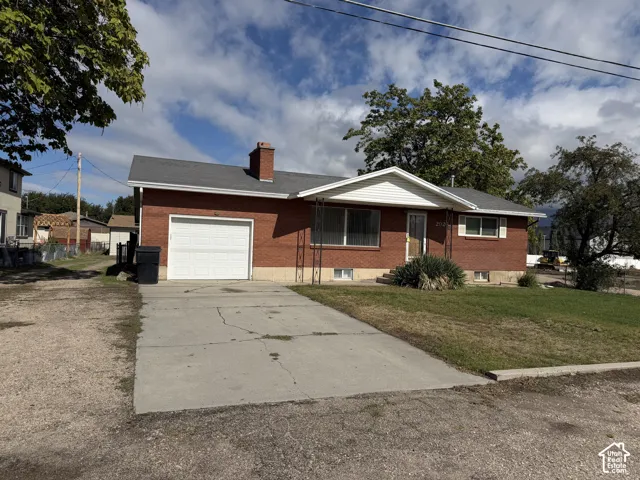 Red brick exterior featuring a shingle roof, attached garage, masonry chimney, and concrete driveway