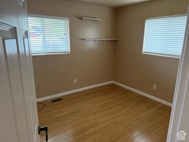 Room featuring wood-finish flooring, two windows with blinds, and built-in wall shelving