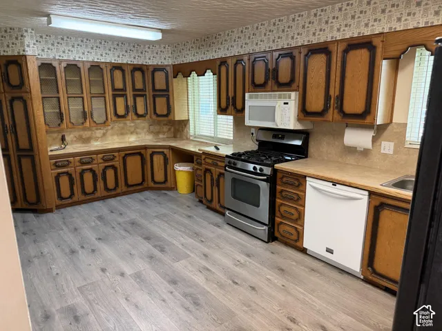 Kitchen featuring custom wood cabinetry with decorative detailing, stone-finish countertops, stainless steel gas range, integrated microwave, and wood-finish flooring