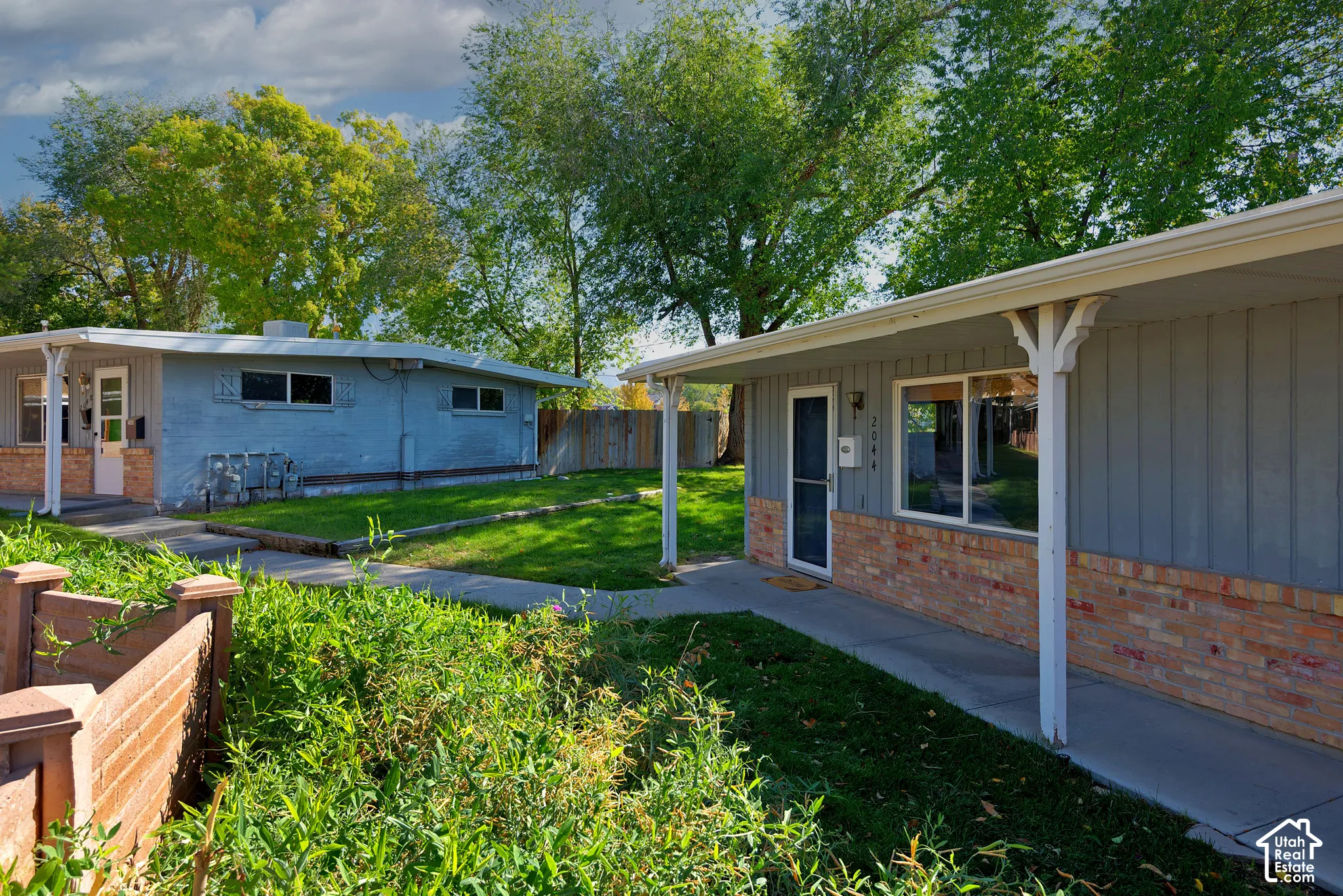Exterior featuring brick and vertical siding, covered walkways, and mature landscaping