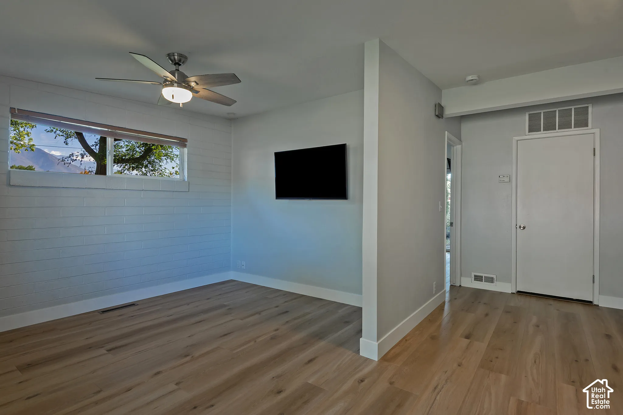 Light-filled room featuring wood-finish flooring, a textured block wall, a multi-blade ceiling fan with integrated light fixture, and horizontal transom window