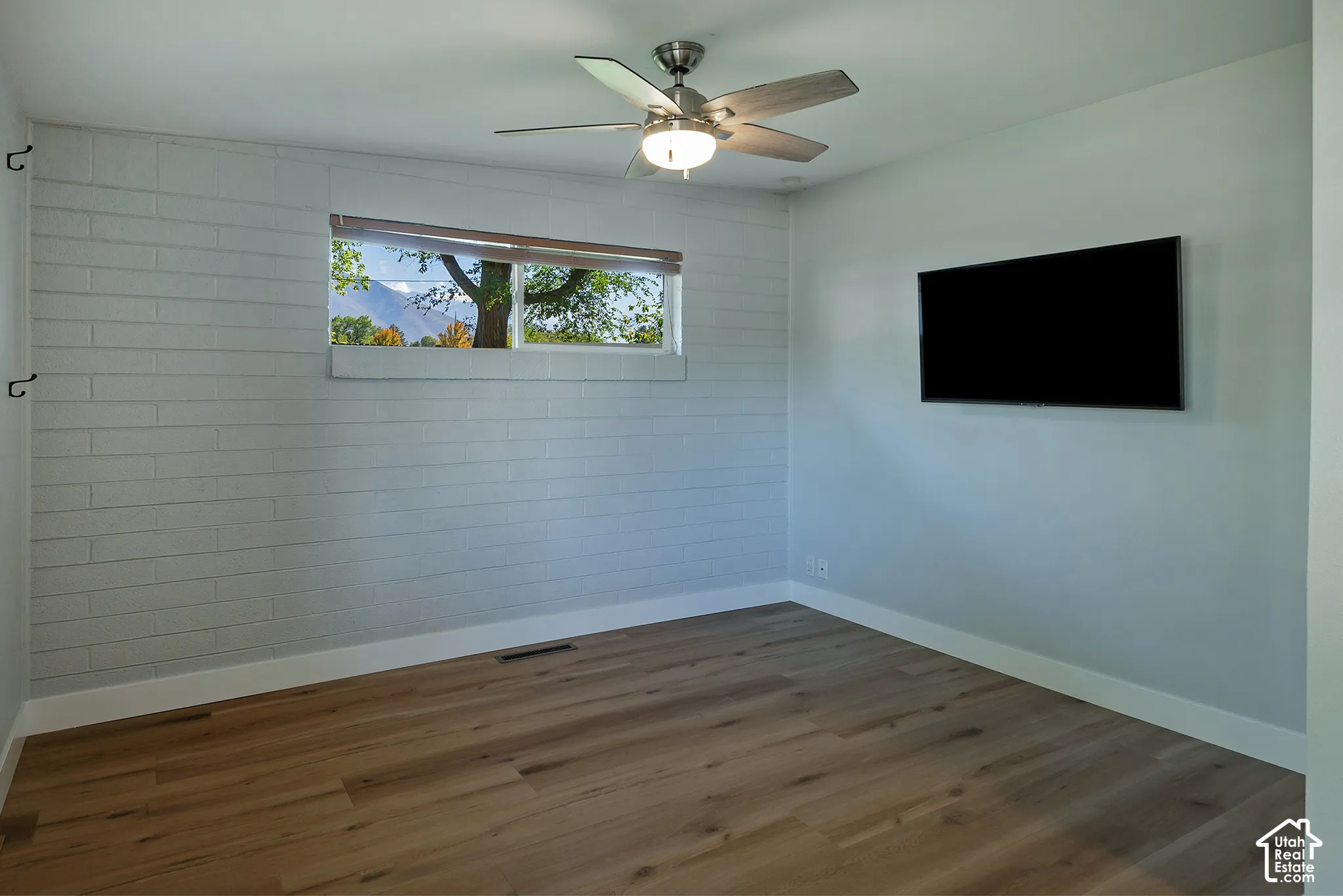 Interior space featuring white-painted masonry wall, wood-finish flooring, and a ceiling-mounted light fixture with fan