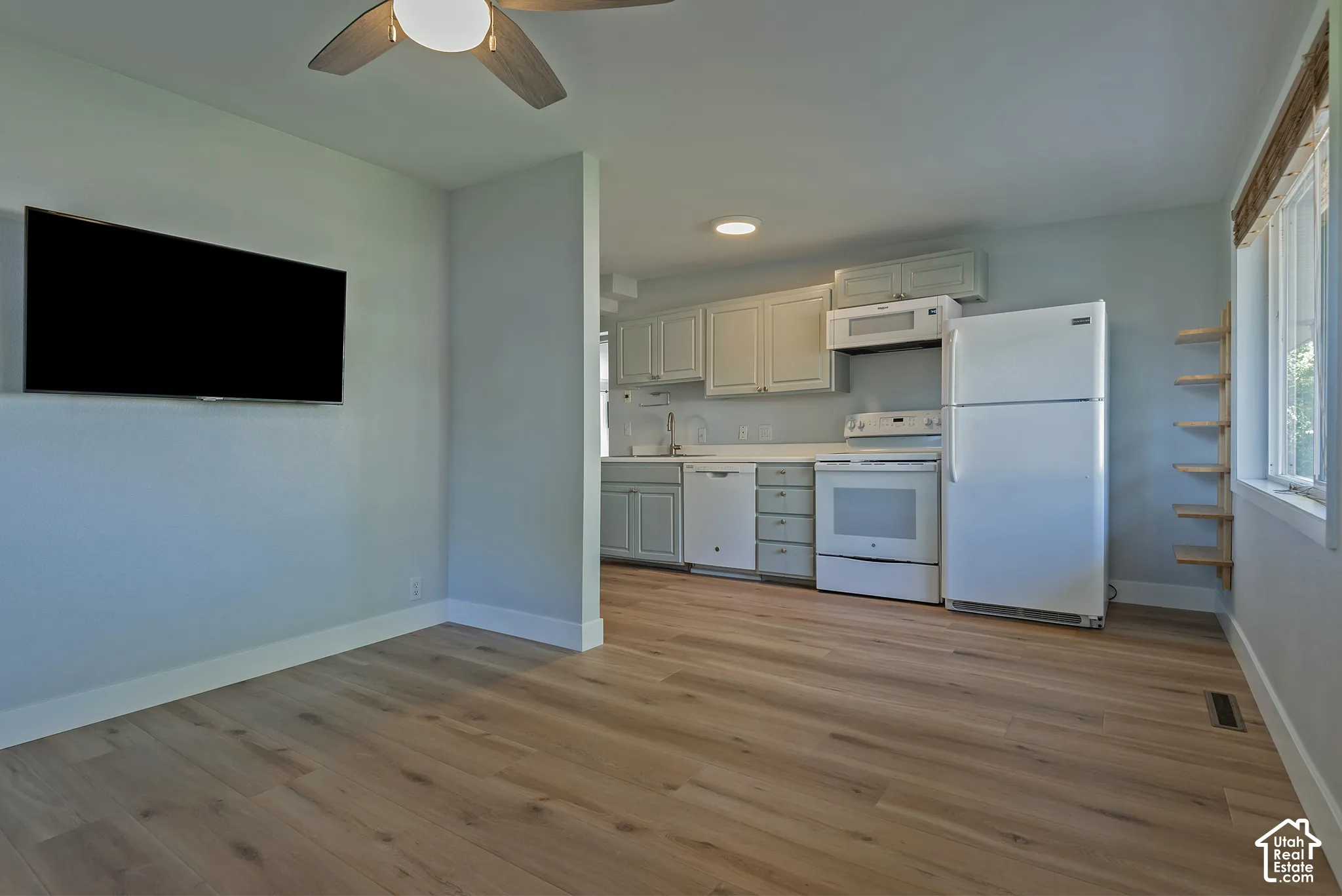 Kitchen featuring shaker-style cabinetry, white appliances, and wood-finish flooring, complemented by a ceiling fan and wall-mounted shelving