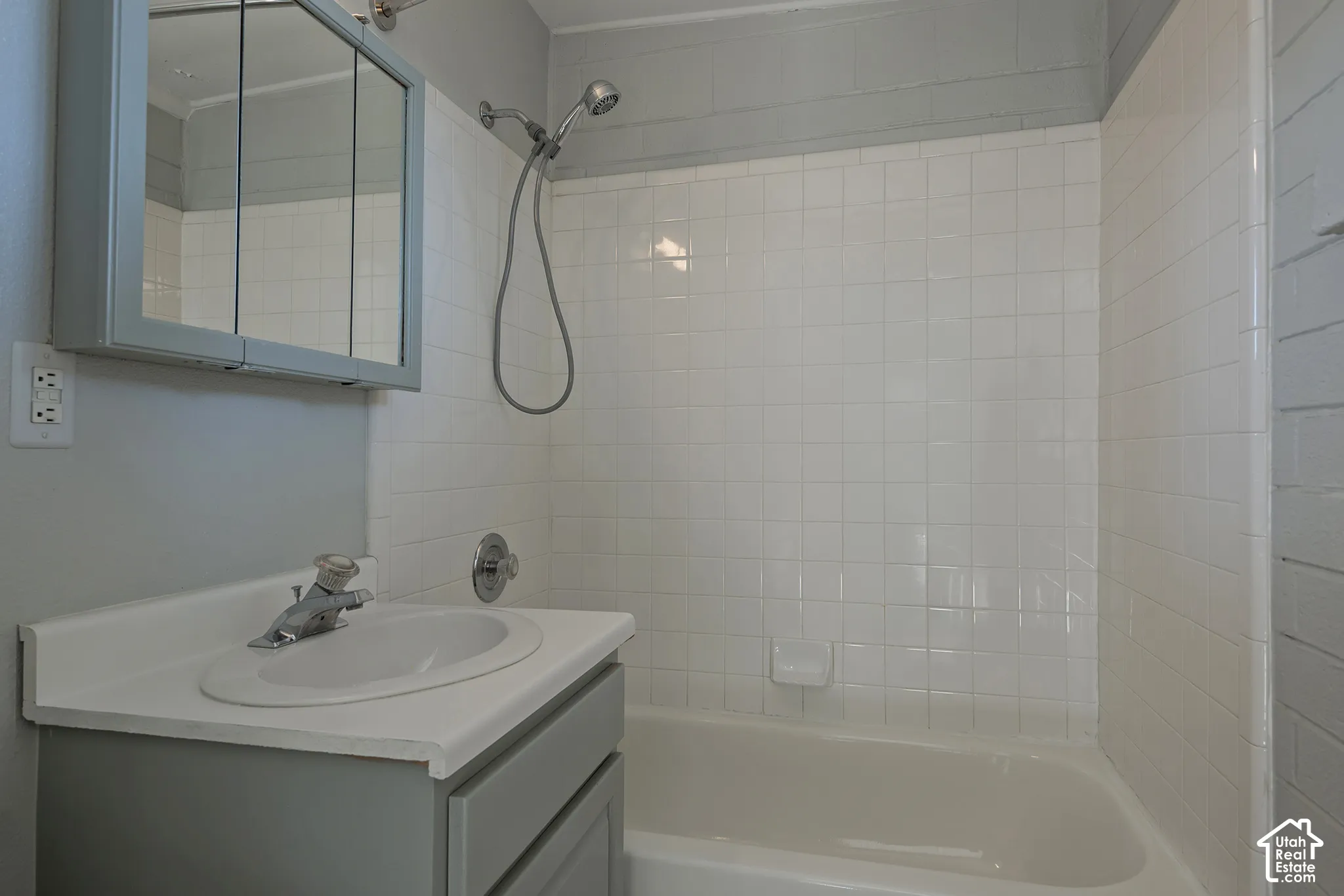 Bathroom featuring a vanity cabinet with a solid surface countertop, integrated sink, mirrored medicine cabinet, and a bathtub enclosure with white square tile surround