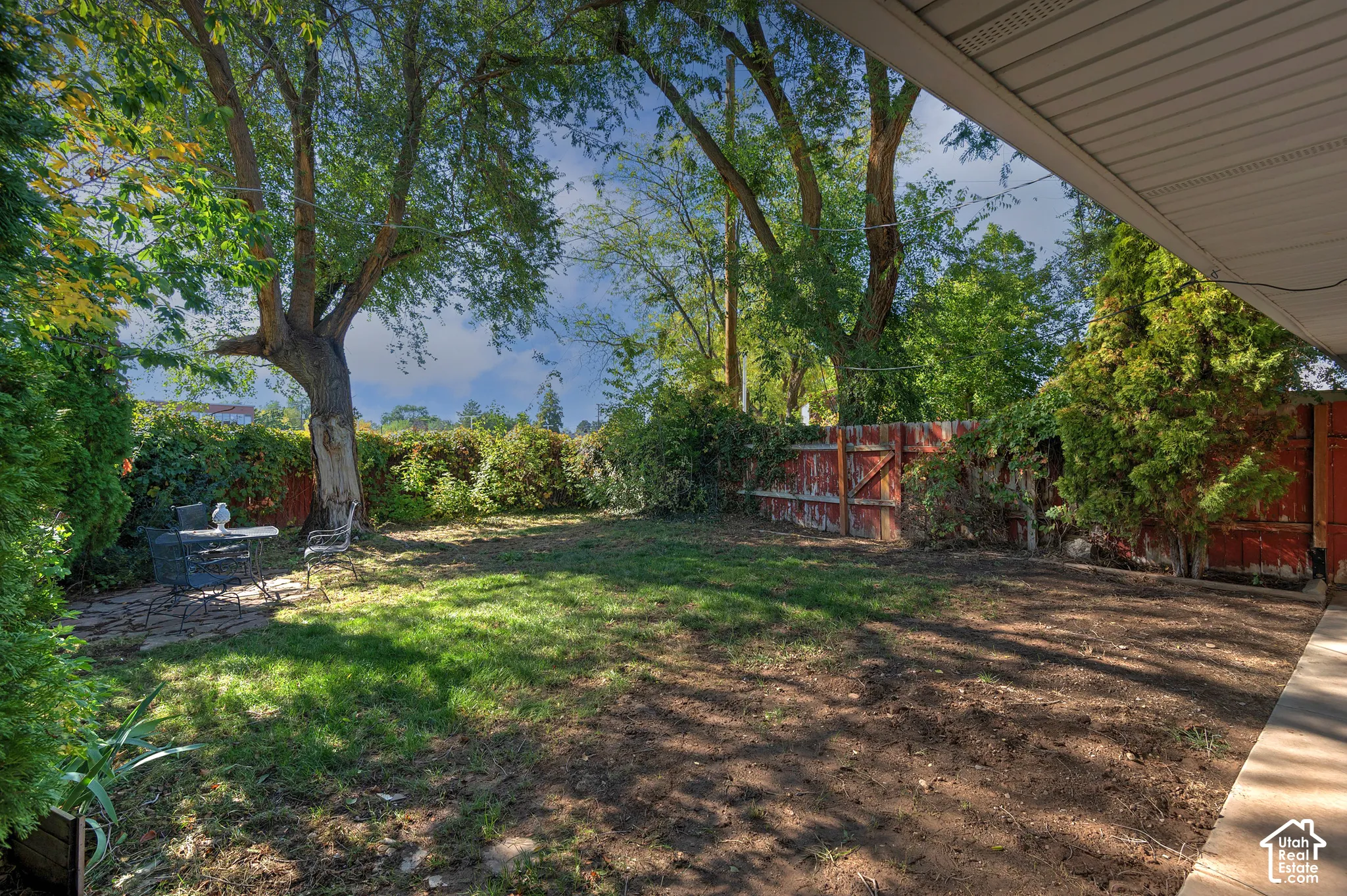 Backyard featuring a stone-paver patio, wood privacy fencing, mature trees, and a covered porch overhang