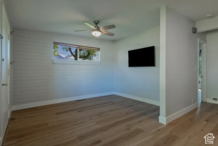 Interior space featuring wood-finish flooring, white painted brick accent wall, and a brushed nickel ceiling fan with integrated lighting