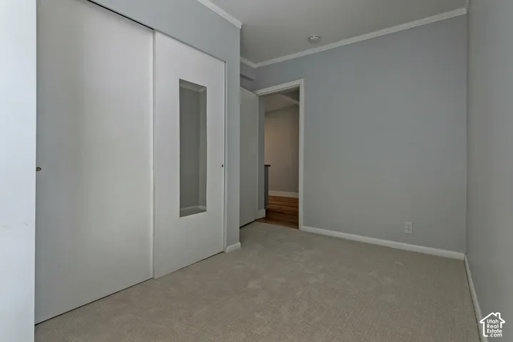 Neutral-toned room featuring plush wall-to-wall carpeting, sliding closet doors with glass panel inserts, and crown molding