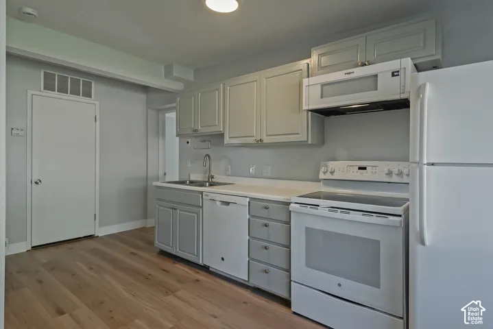 Kitchen featuring shaker-style cabinetry, white appliances including a built-in microwave, wood-finish flooring, and a stainless steel gooseneck faucet