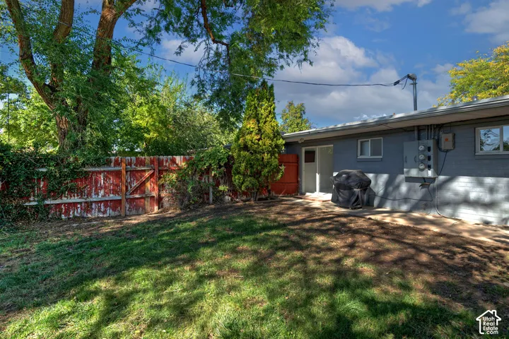 Fenced backyard featuring a grass lawn, mature trees, and an attached masonry exterior