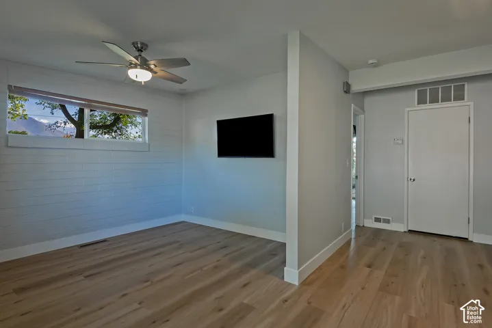 Light-filled room featuring wood-finish flooring, a textured block wall, a multi-blade ceiling fan with integrated light fixture, and horizontal transom window