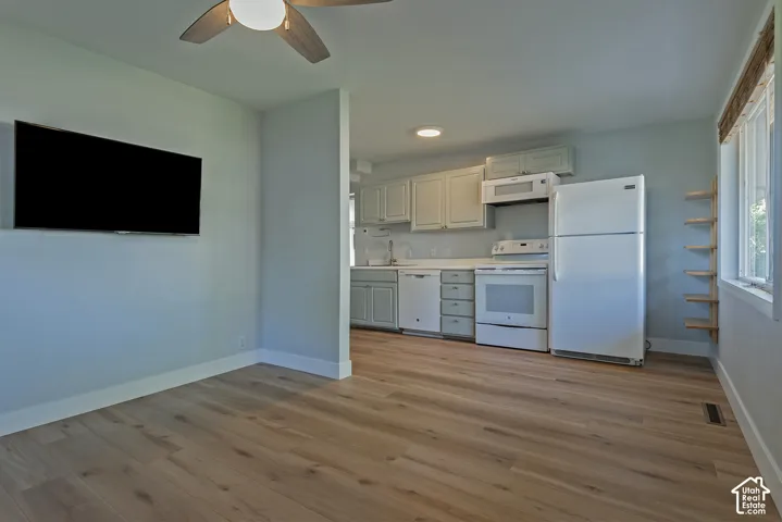 Kitchen featuring shaker-style cabinetry, white appliances, and wood-finish flooring, complemented by a ceiling fan and wall-mounted shelving
