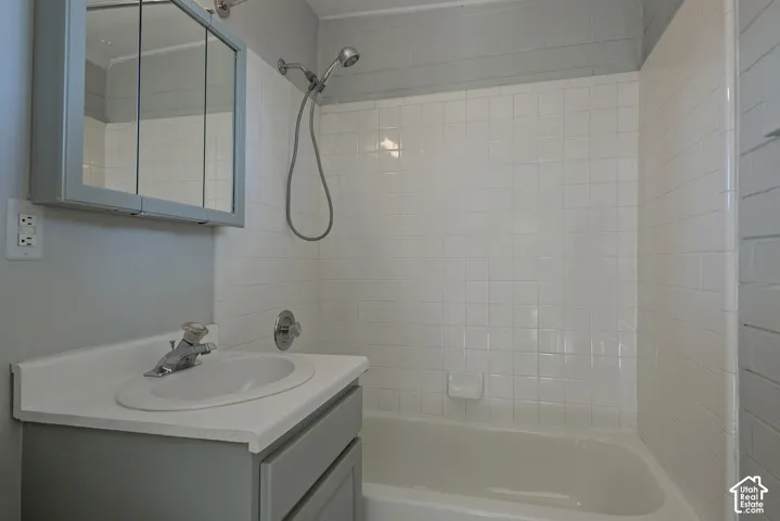 Bathroom featuring a vanity cabinet with a solid surface countertop, integrated sink, mirrored medicine cabinet, and a bathtub enclosure with white square tile surround