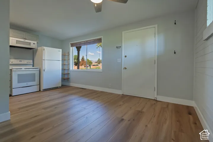 Kitchen area featuring wood-finish flooring, white cabinetry, a built-in microwave, an electric range, and a textured wall panel finish