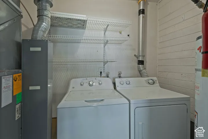 Utility space featuring installed washer and dryer hookups, white wire wall-mounted shelving, and exposed painted masonry walls
