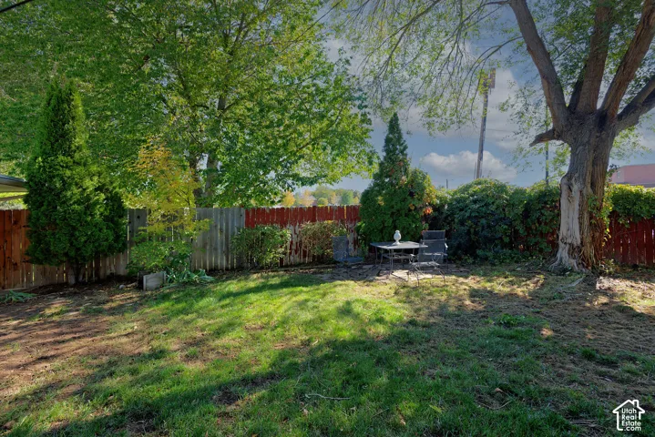 Backyard featuring a grass lawn, perimeter wood fencing, and mature trees