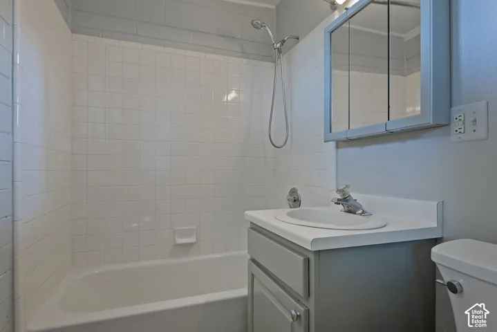 Bathroom featuring a tub-shower combination with white wall tile, a single-basin vanity with a solid-surface countertop, and a tri-fold medicine cabinet