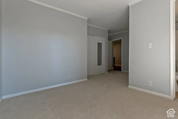 Neutral-toned wall paint, wall-to-wall carpeting, crown molding, and a closet with a glass-paneled door