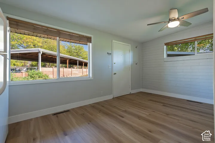 Room with wood-finish flooring, painted brick accent wall, large picture windows, and ceiling fan with integrated lighting