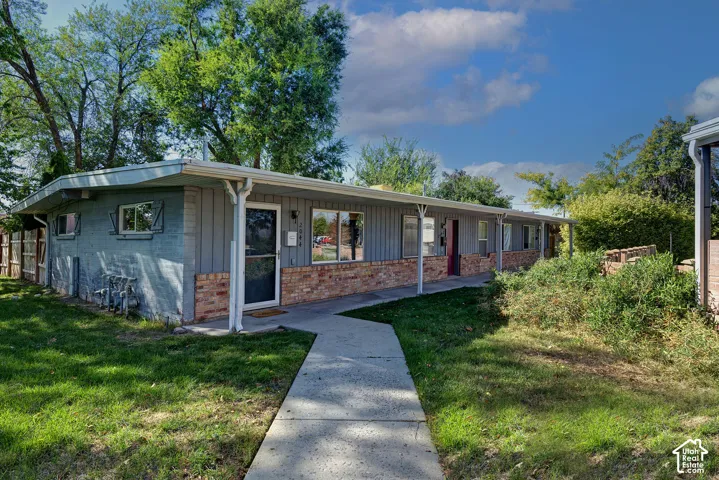 Single-story exterior featuring a mix of vertical wood-style siding and brick masonry, covered entryway, and concrete walkway