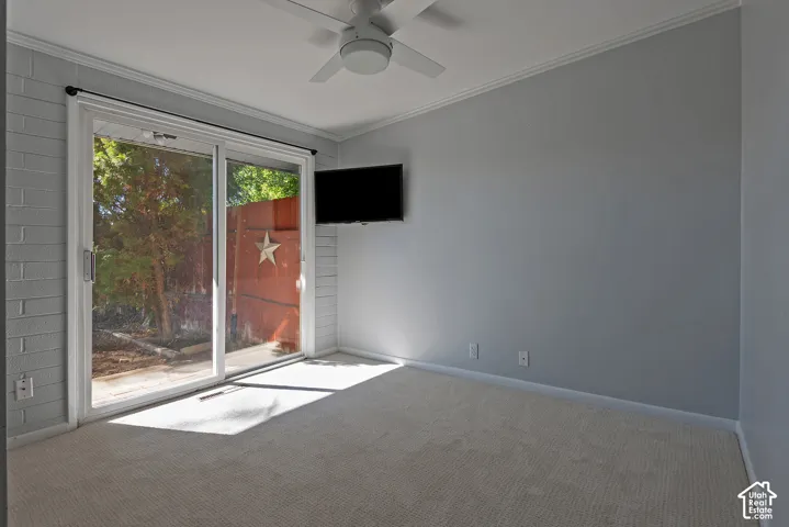 Room featuring white-painted masonry wall, sliding glass door, neutral carpeting, and a ceiling-mounted fan