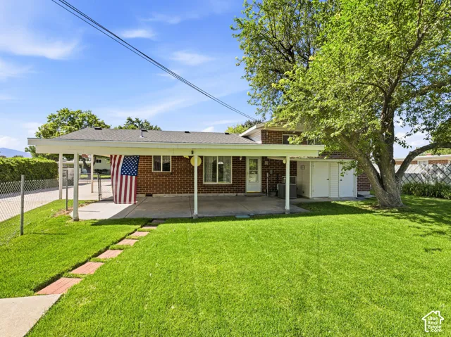 Rear exterior with a covered patio, brick facade, mature trees, and green lawn with a paver path