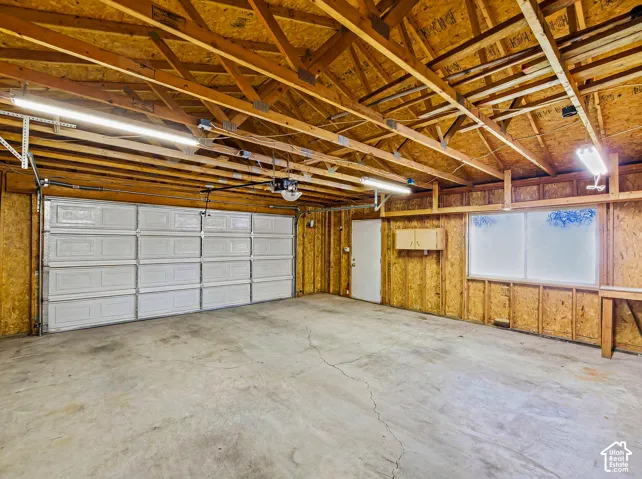 Two-car garage with overhead lighting, exposed wood ceiling joists, and a concrete floor