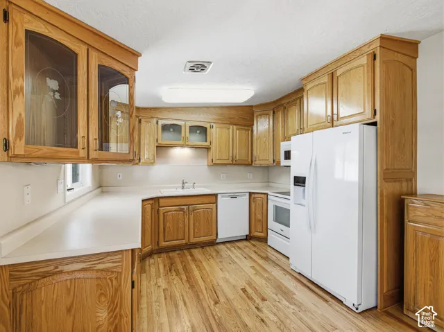 Kitchen featuring wood-finish flooring, white countertops, built-in cabinetry, white appliances, and an integrated double-door refrigerator