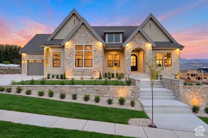 Multi-gabled exterior featuring stone masonry cladding, arched entry portico, concrete steps, and integrated hardscaping with tiered stone retaining walls