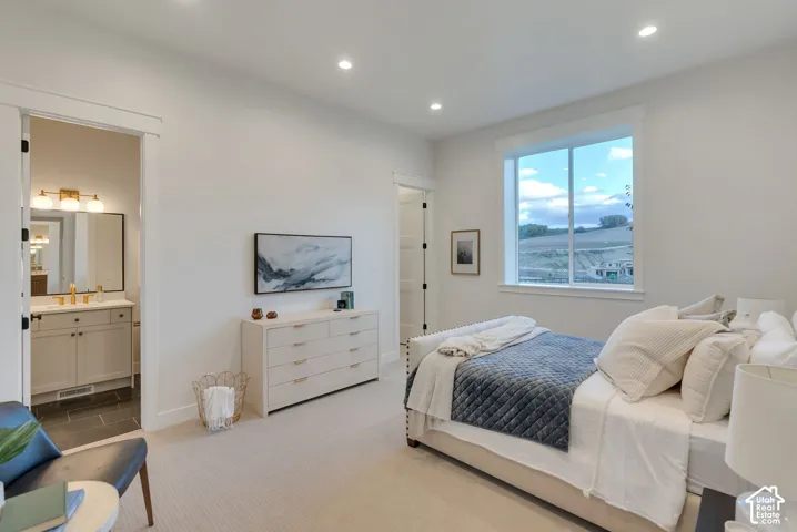 Neutral-toned bedroom featuring recessed lighting, large picture window, and carpeted flooring, with a separate vanity area showcasing a stone countertop and gold-tone fixtures