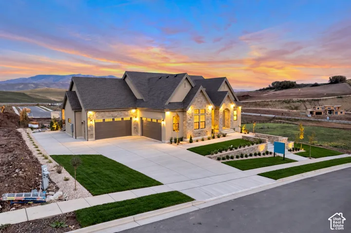 Exterior featuring stone masonry facade, multi-gable roofline, attached three-car garage, concrete driveway, and tiered stone retaining walls