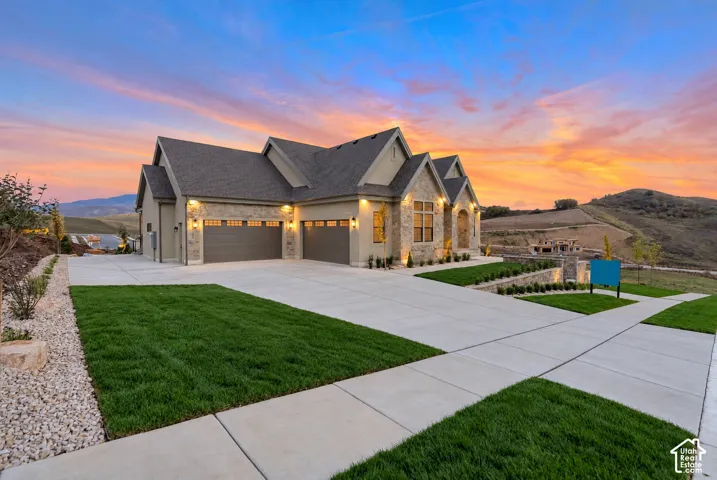Multi-gabled exterior featuring stone facade accents, an expansive concrete driveway, a three-car garage, and a tiered landscaped lawn