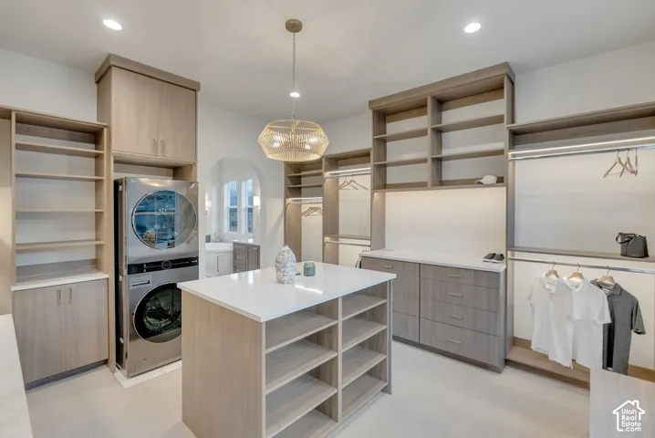 Custom cabinetry with extensive shelving, central island featuring a light-toned solid surface countertop, integrated stainless steel laundry appliances, and decorative drum pendant lighting