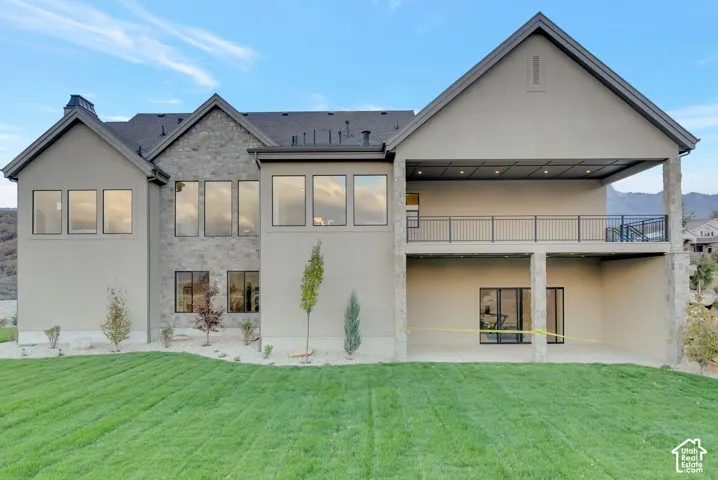 Multi-story exterior featuring natural stone veneer accents, an expansive covered deck with recessed lighting, a ground-level covered patio, and large-format glass windows