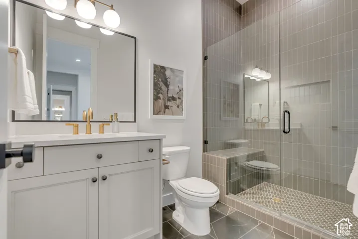 Bathroom featuring a vanity with a countertop, integrated sink, and brass-finish fixtures, complemented by a walk-in shower with a glass enclosure, floor-to-ceiling tile, and a built-in recessed shelf