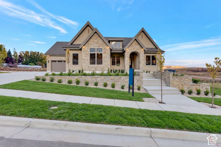 Exterior featuring stone veneer siding, arched entryway, multi-gabled roofline, concrete driveway, and tiered stone retaining walls