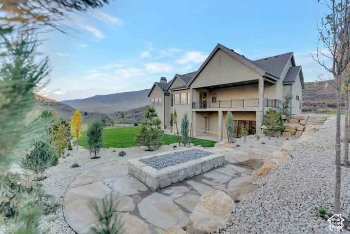 Custom flagstone patio featuring a built-in stone fire pit, tiered landscaping with stone retaining walls, and a raised covered deck with metal railings