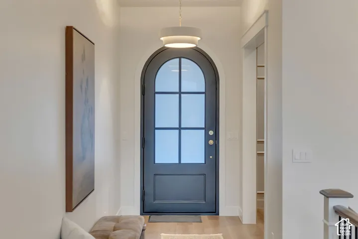 Entryway featuring an arched door with six-pane glass inlay, neutral wall paint, wood-finish flooring, and a multi-tiered circular pendant light