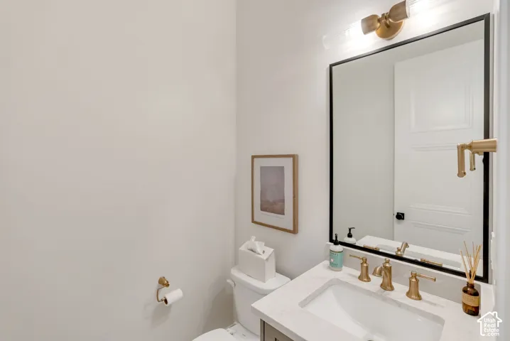 Bathroom featuring a vanity with a white countertop and undermount sink, brass-finish widespread faucet, framed rectangular mirror with a black border, and horizontal wall-mounted light fixture with glass shades