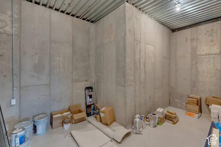Storage room featuring concrete walls and exposed corrugated metal ceiling