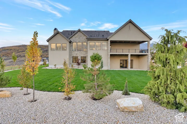 Stucco and stone exterior featuring an elevated covered balcony with a metal railing, multi-pane windows, and a landscaped yard with rock mulch