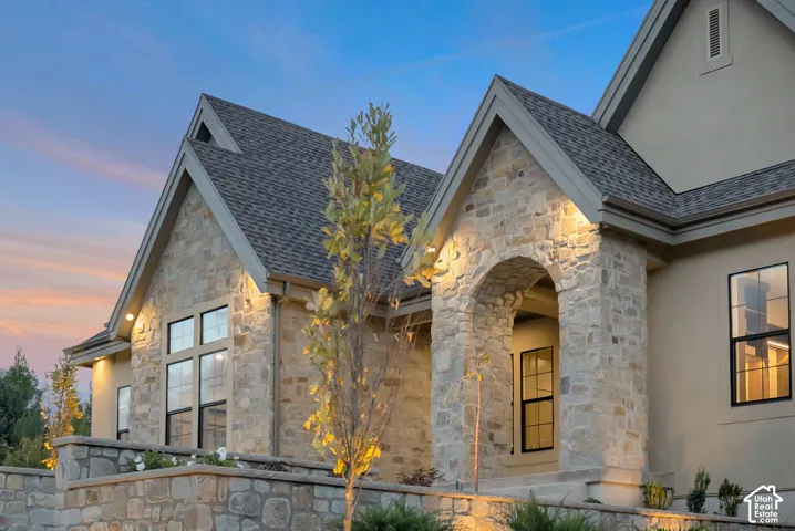 Exterior elevation featuring a stucco finish, stone veneer accents, an arched entryway, multi-pane windows, and a multi-gabled roofline