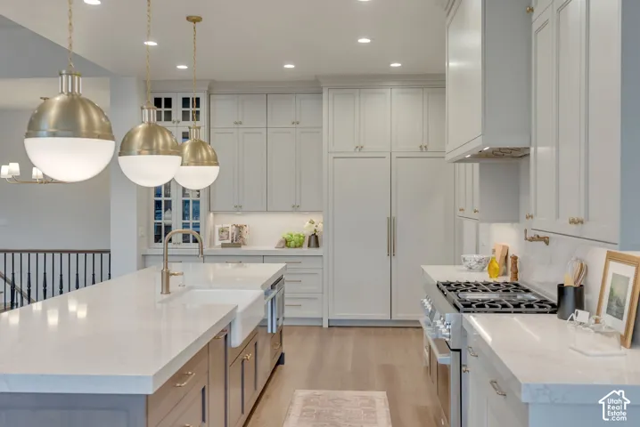 Kitchen featuring a spacious island with a farmhouse sink, stone countertops, custom cabinetry, professional-grade gas range, and statement globe pendant lighting