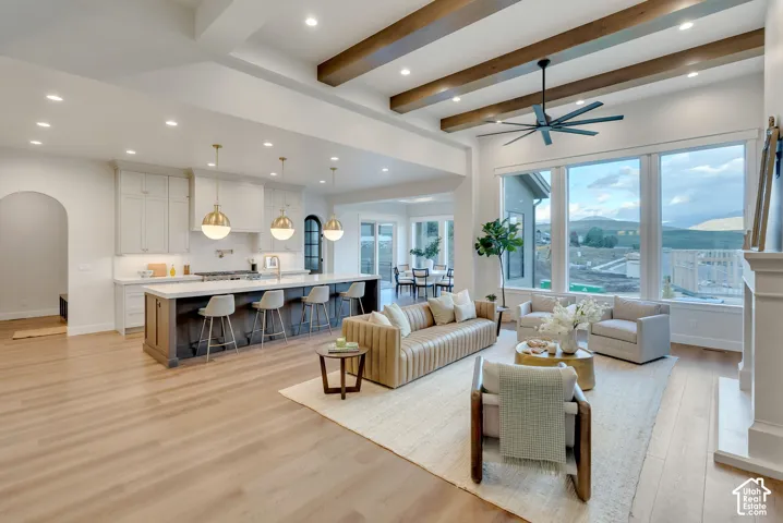 Open-concept interior featuring wood-finish flooring, exposed ceiling beams, a large kitchen island with pendant lighting, recessed lighting, and expansive windows