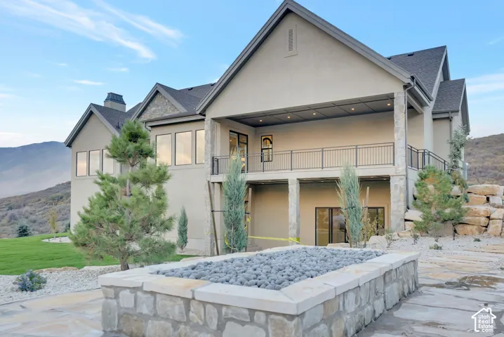Stucco exterior featuring multi-level covered patios, stone-clad pillars, a built-in stone fire feature, and mountain scenery